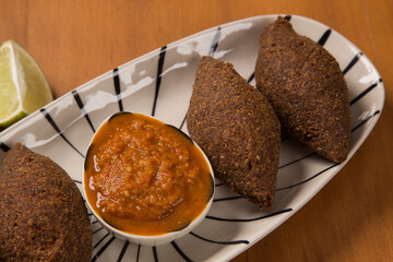 fried kibbeh served with pepper sauce, on a white plate.
