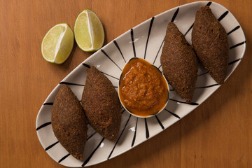 fried kibbeh served with pepper sauce, on a white plate.