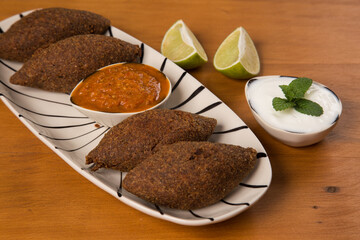 fried kibbeh served with pepper sauce, on a white plate.