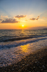 Fototapeta na wymiar Amazing sea sunset on the pebble beach, the sun, waves, clouds