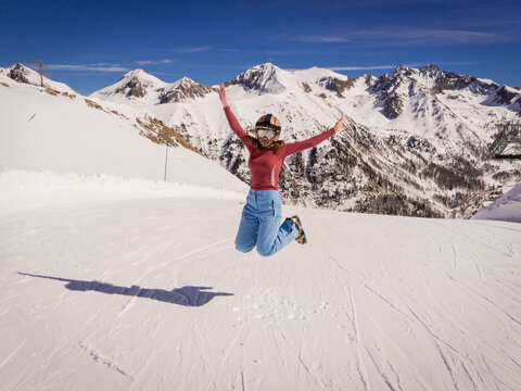 A girl joyfully jumps at the top of the piste in winter at the ski resort of Isola 2000, France