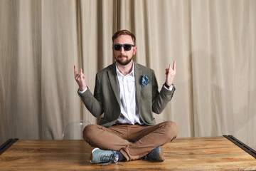 Full length of a relaxed mature young hipster sitting in sunglasses on table at home