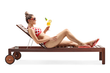 Young woman in bikini lying on a sunbed and holding a cocktail