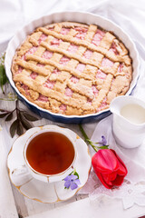 White porcelain cup of tea, and fresh-baked pie. English breakfast still-life with drink and treats red tulip flower and white tablecloth.