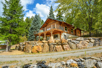 A picturesque rustic log home in the mountains surrounded by pine trees on a rocky hillside in...