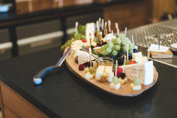 Wooden board with sliced different types of ripened cheese served together with olives, grapes, strawberries and raspberries. Celebration, party