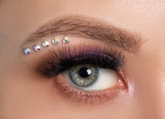 Woman's blue green eye with beautiful make-up and thick eyebrows, crystals under the eyebrow  close...