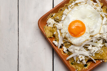 Mexican green chilaquiles with fried egg and cheese on white background