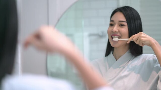 Pretty asian woman brushing her teeth by toothbrush in modern bathroom in morning