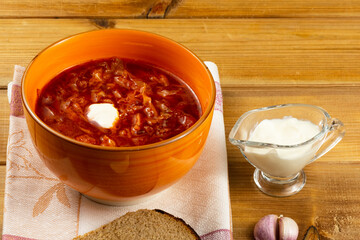 Vegetarian borsch in an orange bowl, sour cream, garlic, rustic bread on a wooden background. Vegetarian food. Healthy lifestyle