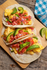 Breakfast egg tacos with flour tortilla and fresh sauce on wooden background