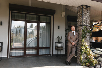 Man in beige checkered suit standing on the terrace of the modern house. Groom portrait