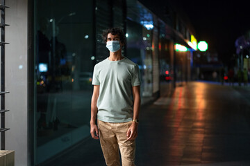 Handsome young man with face mask walks on city street at night