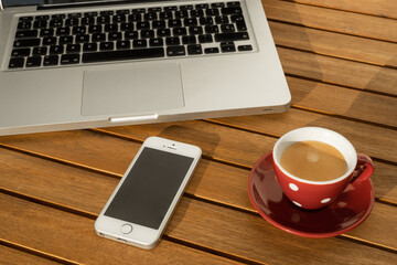 Laptop computer next to cup with coffee and mobile phone, on wooden table in the terrace, working in the confinement.