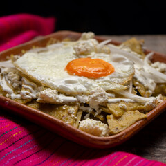 Mexican green chilaquiles with fried egg and cheese on wooden background
