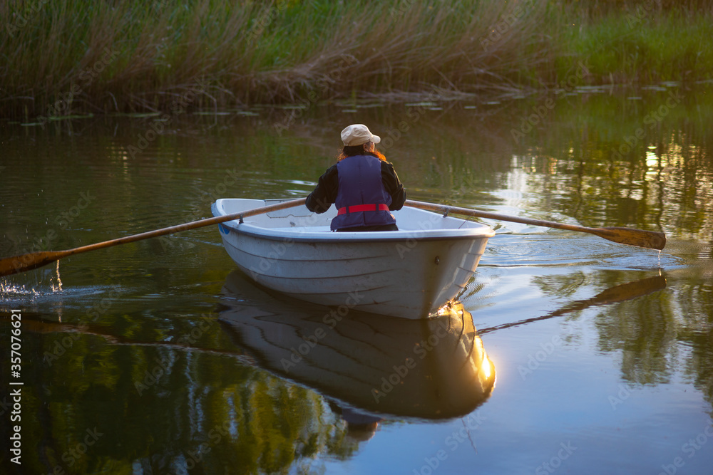 Wall mural Woman with life jacket in rowboat in river in tranquil summer evening