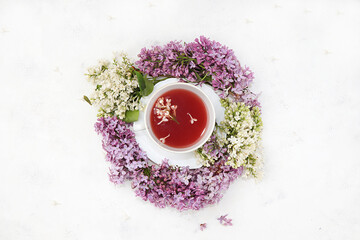 Flower composition. Cup of flower tea with a branch of lilac flowers on a white wooden background, flat lay, concept of healthy eating. Place for text, selective focus
