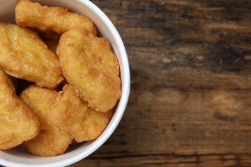 Bucket with tasty chicken nuggets on wooden table, top view. Space for text