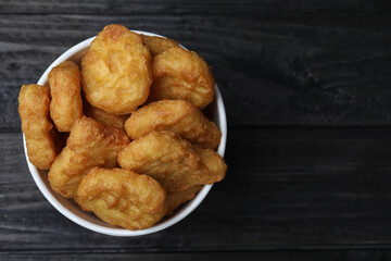Bucket with tasty chicken nuggets on black wooden table, top view. Space for text