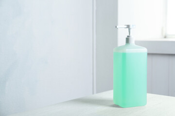 Dispenser bottle with green antiseptic gel on table indoors. Space for text