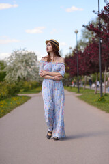 A beautiful girl in a blue dress and a straw hat walks along an empty Boulevard in the city garden....