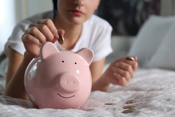 Obraz na płótnie Canvas Woman putting money into piggy bank on bed at home, closeup