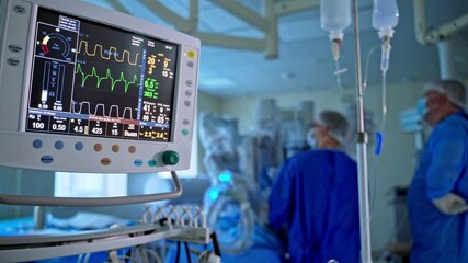 Medical monitor in the hospital. Modern equipment in the operating room on the background of doctors in blue uniform. Screen displays patient's vital signs.