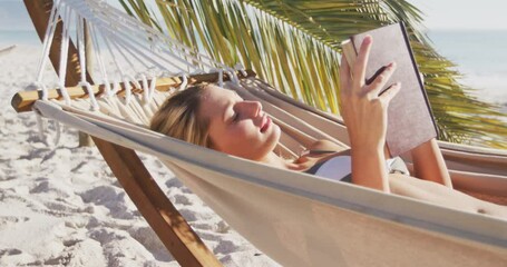 Caucasian woman lying on a hammock and reading a book on the beach