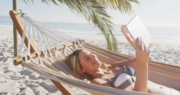 Caucasian woman lying on a hammock and using her tablet on the beach