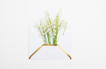 Bright floral flat lay with lily of the valley flowers and white envelope with golden elements