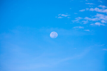 Day moon against a blue sky with Cirrus Cumulus clouds.