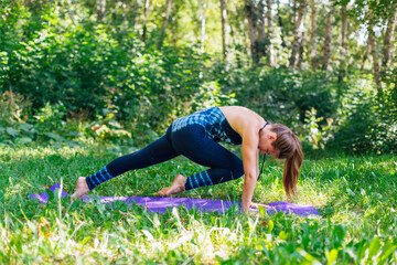 Fototapeta premium Young woman doing yoga exercises in summer city park.