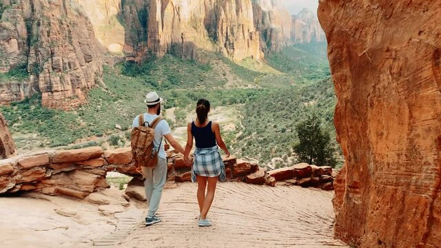 Following a couple of travelers walking by touristic roads around the Grand Canyon in Arizona, traveling around United States, green lands between red rocky cliffs of canyon