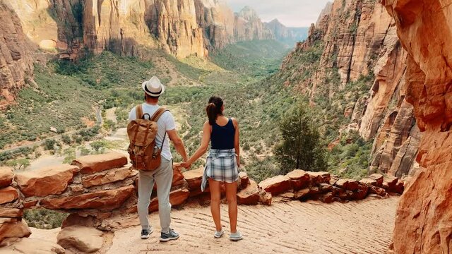 Following a couple of travelers walking by touristic roads around the Grand Canyon in Arizona, traveling around United States, green lands between red rocky cliffs of canyon