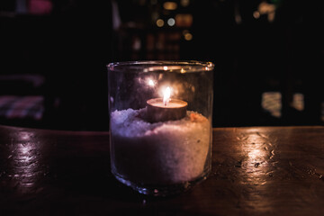 Isolated tealight inside a glass illuminating a dark scene and reflections on a wooden table and a nice bokeh background
