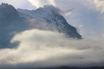 Foggy day with with the Alps in the background and person falling down with air hot balloon.