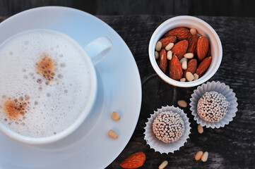 cappuccino Cup with almonds, pine nuts and round chocolates on a wooden surface