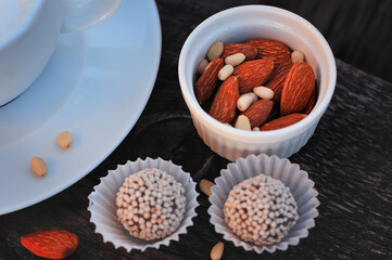 cappuccino Cup with almonds, pine nuts and round chocolates on a wooden surface