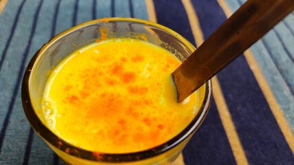Turmeric mixed milk glass with spoon, close up image