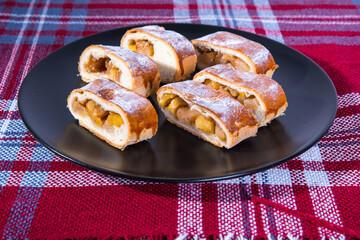 Strudel with apples, sliced ​​on a black plate, red tablecloths, close-up