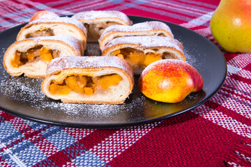 Strudel with apples, sliced ​​on a black plate with peach red tablecloths, close-up