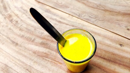 Turmeric mixed milk glass with spoon on the wood table