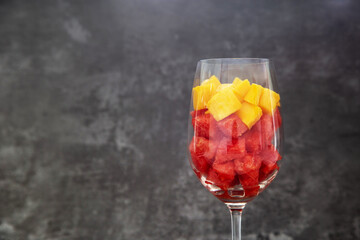 Pieces of yellow mango and red watermelon in glass.