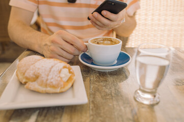 Close up of man having breakfast  and using mobile phone on summer terrace  at home on sunny day. 