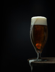 Glass of cold fresh beer with leaky foam on wooden table on black background.Close up.