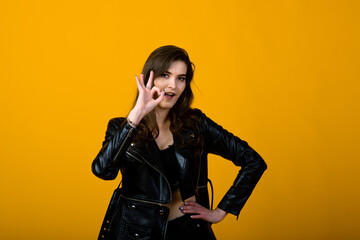 Portrait of a happy young brunette girl showing gestures and smiling, surprising isolated over yellow background. Emotional picture.