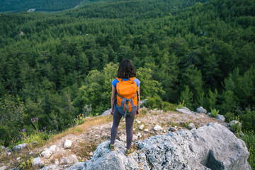 Fototapeta na wymiar A woman with a backpack stands on top of a mountain and admires the beauty of a mountain valley.