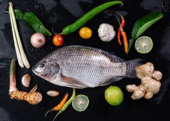 Delicious fresh fish on dark background. Fish with aromatic herbs, spices and vegetables - healthy food, diet or cooking concept