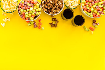 Top view of flavored popcorn and soda on yellow desk from above copy space