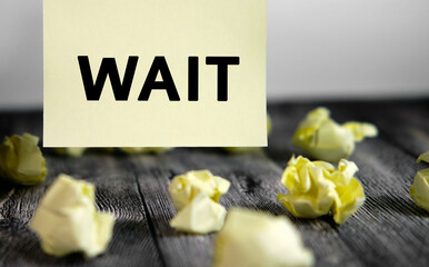 Wait - text on yellow note sheets on a dark wooden background with crumpled sheets